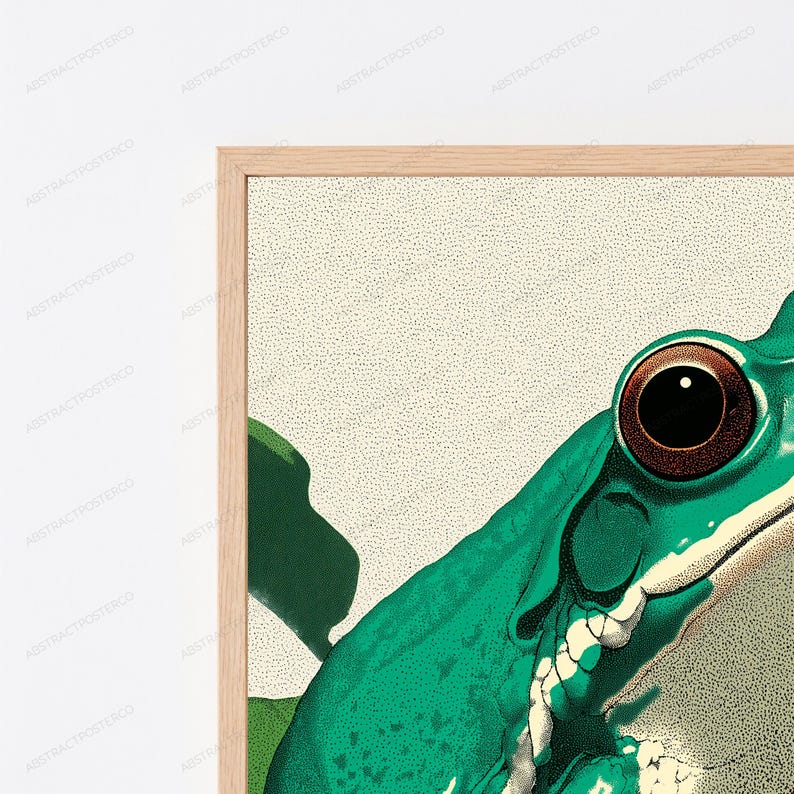 Może przedstawiać: Oprawiony wydruk ścienny przedstawiający ilustrację zielonej żaby w zbliżeniu z dużym, ciemnobrązowym okiem. Żaba znajduje się na jasnokremowym tle o kropkowanej fakturze, zamknięta w ramie z jasnego drewna.