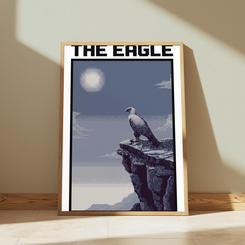 May include: A framed pixel art print titled THE EAGLE, featuring a white and dark grey eagle perched on a jagged cliff edge against a blue sky with a pale sun and clouds. The artwork uses a blocky, digital aesthetic with a muted colour palette.