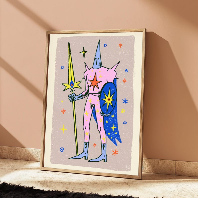 May include: A framed art print featuring a stylised illustration of a figure in a pink suit with a pointed hood, holding a long yellow spear and a blue shield. The figure is adorned with star motifs against a light purple background with scattered stars.