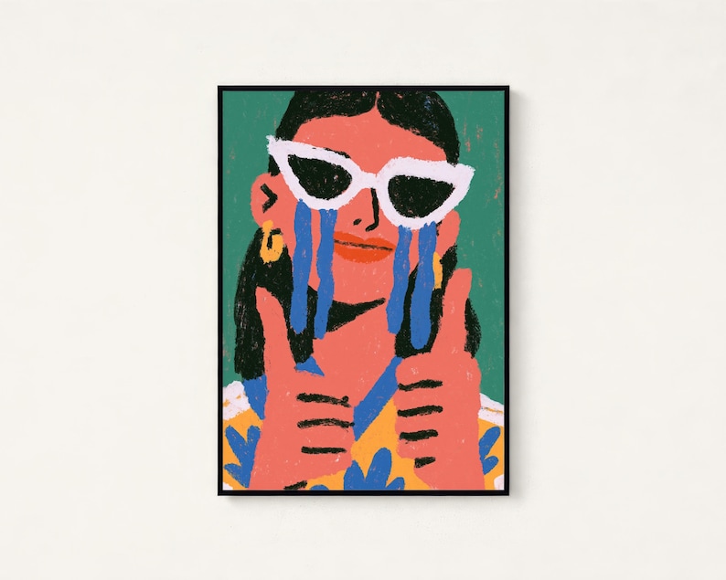 May include: A framed art print featuring a stylized illustration of a person with dark hair wearing white cat-eye sunglasses. The person has blue tears streaming down their face, is wearing a yellow patterned shirt, and is giving two thumbs up.