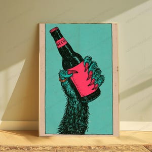 May include: A rectangular art print featuring a stylised illustration of a furry, clawed hand holding a dark beer bottle. The background is a solid teal colour, while the bottle label and the hand's sharp claws are rendered in a vibrant, solid pink.