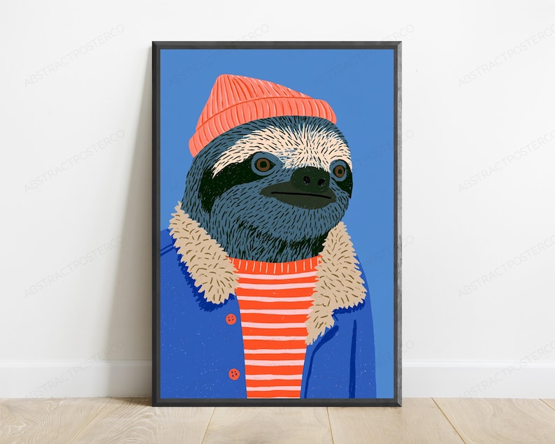 May include: A framed wall art print featuring a stylized illustration of a sloth wearing a coral-colored beanie, a blue jacket with a beige faux-fur collar, and a red and white striped shirt against a solid blue background.