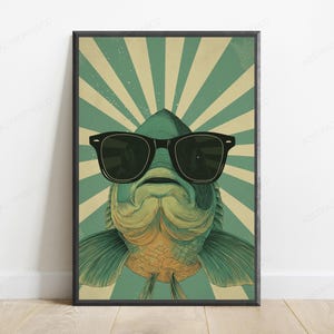 May include: A framed vertical poster featuring a stylized illustration of a fish wearing large black sunglasses. The fish is centered against a background of alternating sage green and cream-colored sunburst rays, creating a graphic design.