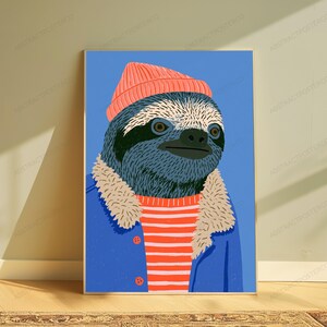 May include: A vertical wall art print featuring a stylized illustration of a sloth wearing a coral-colored beanie, a blue jacket with a beige faux-fur collar, and a red and white horizontal striped shirt against a solid blue background.