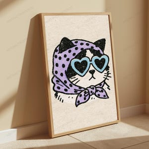 Pu&ograve; includere: Una stampa artistica da parete incorniciata con l'illustrazione di un gatto bianco e nero. Il gatto indossa un foulard viola chiaro a pois neri e occhiali da sole azzurri a forma di cuore su uno sfondo testurizzato color bianco sporco.