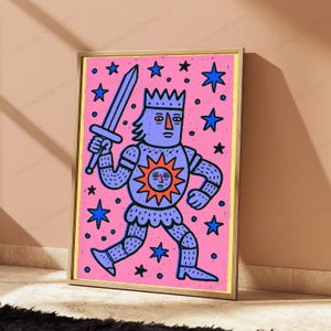 May include: A framed art print featuring a stylized purple knight in armor holding a sword, set against a bright pink background with blue stars. The knight wears a crown and has a sun emblem on the chest with a face, all outlined in bold black lines.