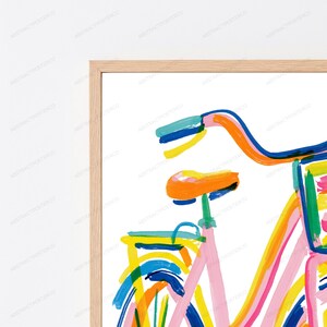 May include: A framed wall art print featuring a stylized, abstract bicycle illustration. The artwork uses bold, expressive brushstrokes in vibrant colors including orange, pink, yellow, blue, and green against a clean white background.