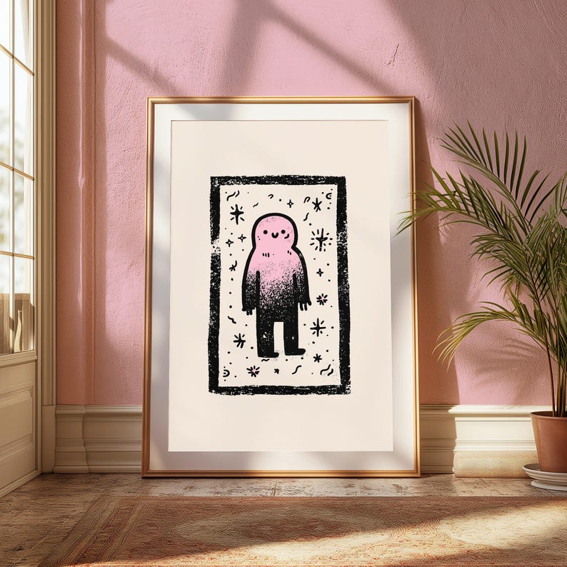 May include: A framed art print featuring a central illustration of a small, smiling creature with a pink head that fades into a black body. The figure is enclosed in a rectangular black border surrounded by various star and squiggle shapes.