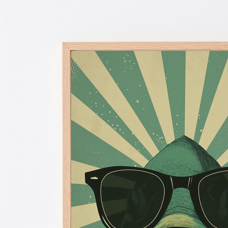 May include: A framed wall art print featuring a green creature wearing black sunglasses. The background consists of a radiating sunburst pattern in alternating shades of muted green and cream, with subtle speckled texture throughout the design.