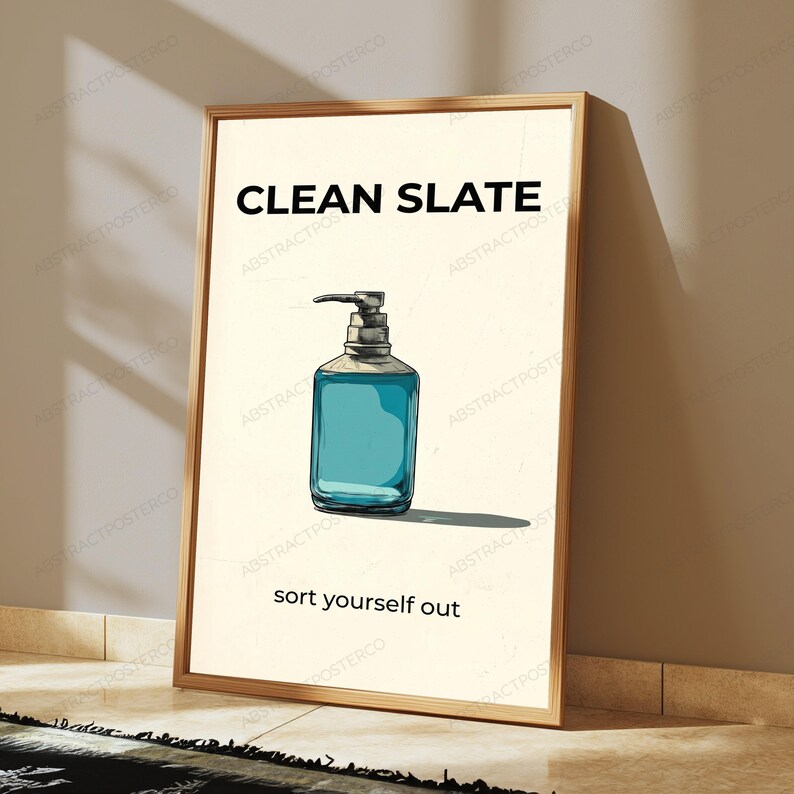 May include: A rectangular framed wall art print featuring a cream-colored background with a central illustration of a blue liquid soap dispenser. The text CLEAN SLATE appears in black at the top, and the text sort yourself out is at the bottom.