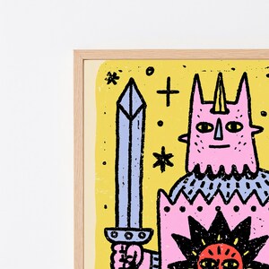 May include: A framed art print featuring a pink horned character holding a blue sword. The character wears a blue patterned tunic and a pink shield with a black sun graphic. The background is yellow with black stars and plus signs.