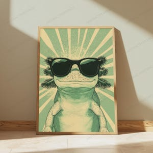 May include: A framed poster featuring a light green axolotl wearing black sunglasses. The axolotl is centered against a background of radiating light green and cream-colored sunburst lines. The illustration has a textured, vintage-inspired aesthetic.