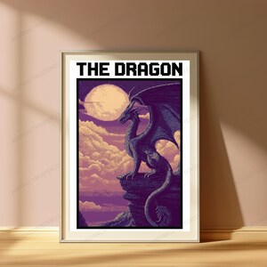 May include: A framed poster featuring pixel art of a dragon perched on a rocky cliff. The scene includes a large pale moon, purple clouds, and a dark landscape. The text THE DRAGON is printed in bold black capital letters at the top of the print.