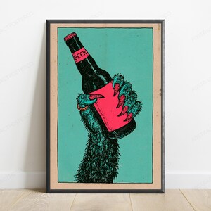 May include: A framed poster featuring a dark, furry creature's hand with sharp claws holding a black beer bottle. The bottle has a bright pink label with the word BEER printed in black. The background is a solid teal colour with a tan border.
