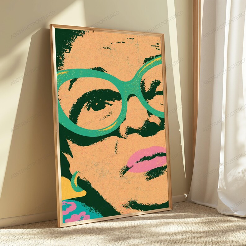 May include: A framed vertical art print featuring a stylized, high-contrast portrait of a person wearing large, bright green glasses. The image uses a peach-toned background with dark green shadows, a vibrant pink mouth, and a yellow earring detail.