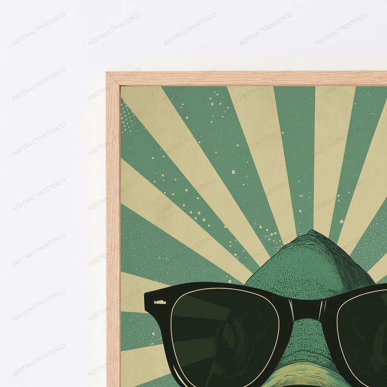 May include: A framed wall art print featuring a green creature wearing black sunglasses. The background displays a sunburst pattern with alternating light beige and muted green rays, accented by small white dots across the entire surface.