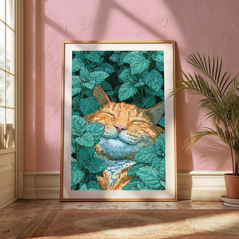 May include: A framed wall art print featuring an orange tabby cat with eyes closed in a contented expression, nestled among dense, vibrant teal-colored mint leaves. The artwork is displayed in a thin gold frame against a soft pink wall.
