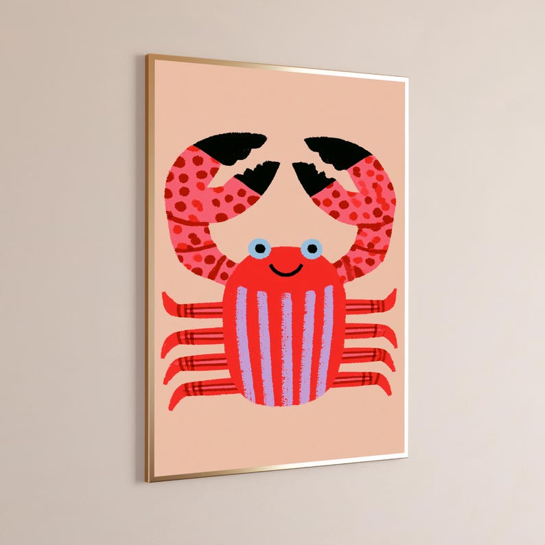 May include: A framed wall art print featuring a stylized crab illustration on a light peach background. The crab has a bright red body with vertical purple stripes, red and pink spotted claws with black tips, and two light blue circular eyes.