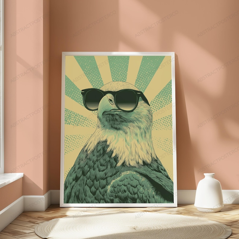 May include: A rectangular wall art print featuring a stylized illustration of a bald eagle wearing black sunglasses. The eagle is centered against a background of alternating light yellow and muted green sunburst rays with a dotted texture pattern.