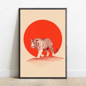 May include: A framed wall art print featuring a tiger illustrated in dark red lines walking across a curved horizon line. Behind the tiger is a large, solid red circle set against a light beige background. The frame is thin and black.