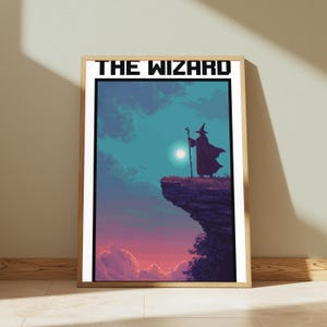 May include: A framed pixel art print titled THE WIZARD, featuring a silhouette of a robed figure with a staff standing on a cliff edge against a teal and purple sky with a bright moon, all enclosed in a light-colored wooden frame.
