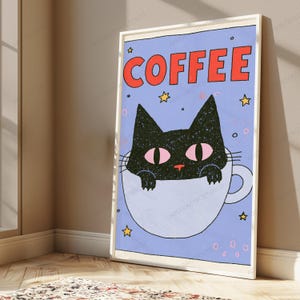 May include: A framed wall art print featuring a black cat with pink eyes peeking out of a light blue coffee mug. The background is a light purple color with small yellow stars and pink circles. The word COFFEE is printed in large red letters.