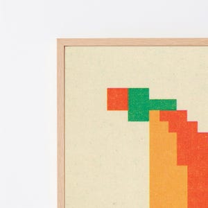 K&ouml;nnte beinhalten: Ein gerahmter Wandkunstdruck mit einem verpixelten Grafikdesign auf hellcremefarbenem Hintergrund. Das Kunstwerk zeigt eine Reihe gestapelter geometrischer Bl&ouml;cke in leuchtenden Orange-, Rot- und Gr&uuml;nt&ouml;nen, eingefasst in einen hellen Holzrahmen.