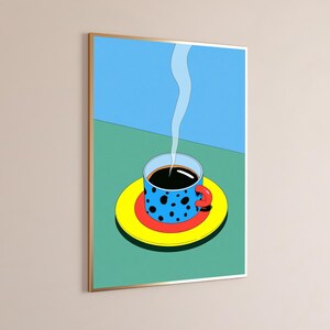 May include: A framed wall art print featuring a blue coffee cup with black polka dots and a red handle, resting on a red and yellow saucer. A thin white wisp of steam rises from the dark coffee against a split blue and green background.