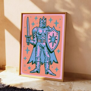 May include: A framed print featuring a stylized illustration of a knight in blue armor against a peach background. The knight wears a crown, holds a sword in the right hand, and carries a shield with a star emblem. Blue stars surround the figure.