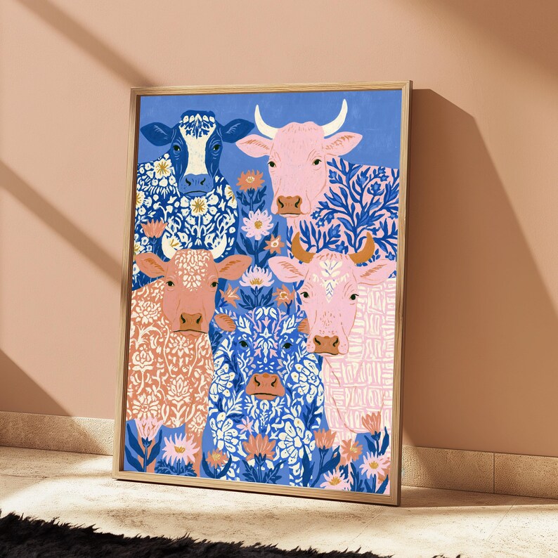 May include: A rectangular wall art print in a light wood frame featuring a colourful illustration of four cows. The cows are depicted in shades of blue, pink, and peach, adorned with intricate floral and geometric patterns, surrounded by small flowers.
