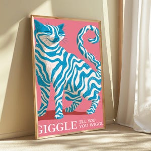 May include: A framed vertical art print featuring a stylised cat with blue and white wavy stripes against a solid pink background. The cat has a curved tail and a smiling expression. The text GIGGLE TILL YOU WIGGLE is printed in white at the bottom.