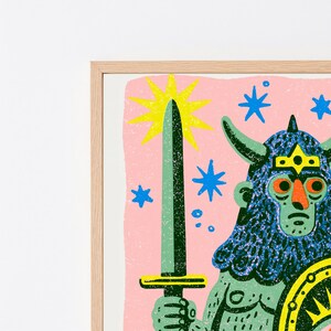 May include: A framed art print featuring a green horned figure with a textured blue helmet, holding a long sword. The background is light pink with a large yellow star and several smaller blue stars. The figure wears a yellow crown and holds a shield.