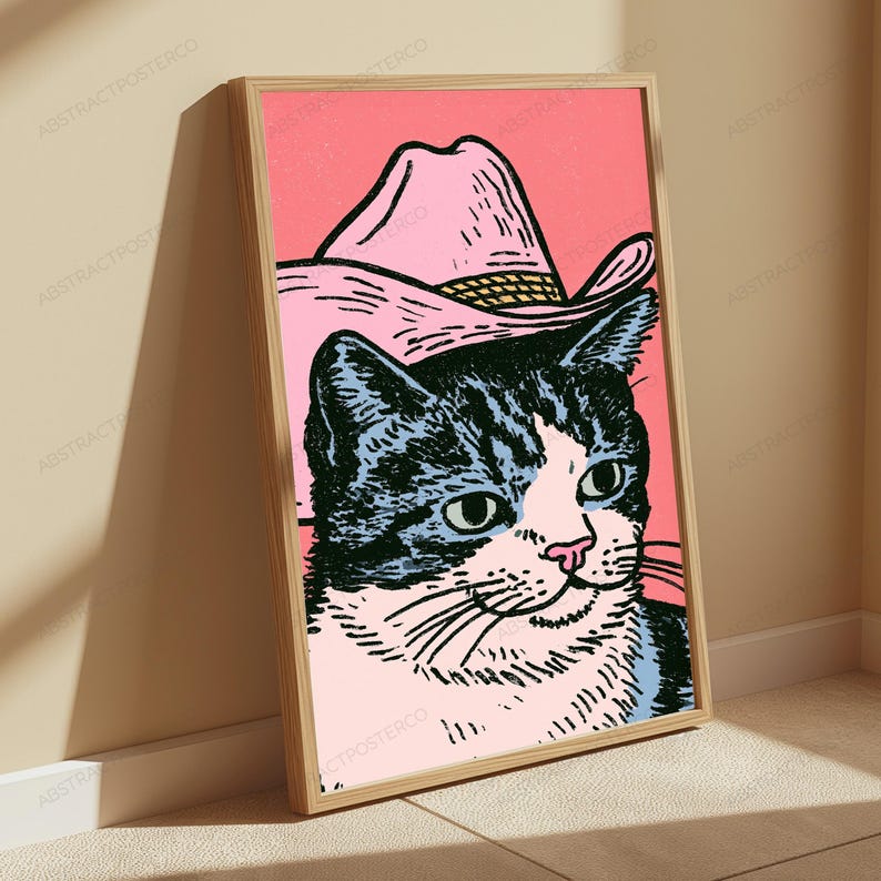May include: A framed wall art print featuring a black and white cat wearing a pink cowboy hat against a solid pink background. The illustration uses bold black ink lines to define the cat's facial features and the texture of the hat.