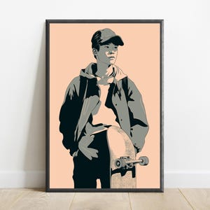 May include: A framed graphic art print featuring a stylized illustration of a person wearing a baseball cap, hoodie, and jacket, standing while holding a skateboard. The artwork uses a palette of peach, black, and grey tones with high contrast.