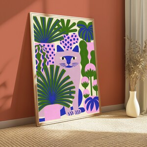 May include: A framed wall art print featuring a light purple cat sitting among various potted plants. The illustration uses a vibrant color palette of green, pink, and blue, with stylized foliage, polka-dot patterns, and rounded plant shapes.