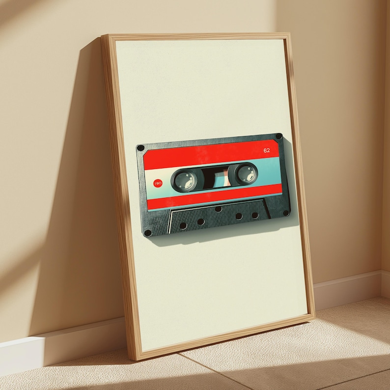May include: A framed vertical wall art print featuring a graphic illustration of a cassette tape. The tape has a black outer shell, a bright red central band, and a light blue middle section. The number 62 is printed in white on the red band.