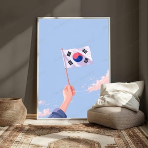 May include: A framed vertical wall art print depicting a hand holding a small South Korean flag against a light blue sky with soft pink clouds. The flag features a white background, a central red and blue taegeuk, and four black trigrams.