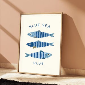 Pode incluir: Uma impress&atilde;o art&iacute;stica emoldurada com tr&ecirc;s peixes orientados horizontalmente com riscas verticais azuis e azul-escuras. Os peixes est&atilde;o dispostos numa coluna sobre um fundo creme. O texto BLUE SEA est&aacute; impresso acima e CLUB abaixo.