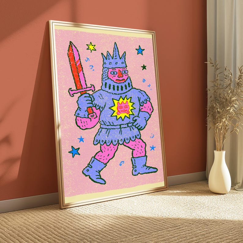 May include: A framed wall art print featuring a stylized illustration of a knight in blue armor and a crown, holding a red and orange sword. The knight has pink skin and a yellow sun emblem on the chest, set against a textured light pink background with scattered blue, green, and yellow stars.