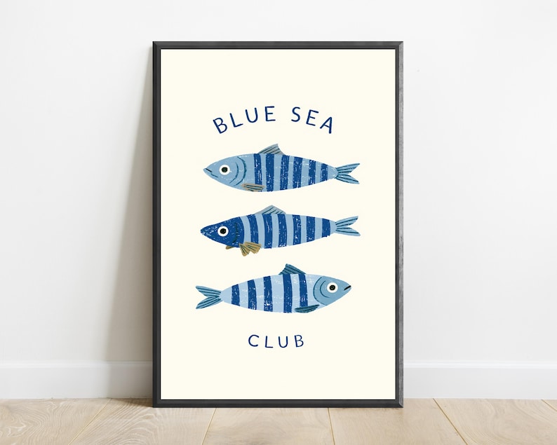 Pode incluir: Uma impress&atilde;o de arte emoldurada apresentando tr&ecirc;s peixes orientados horizontalmente com listras verticais azuis e azul-claras. O texto "BLUE SEA" est&aacute; impresso em azul escuro acima dos peixes e a palavra "CLUB" est&aacute; abaixo deles.