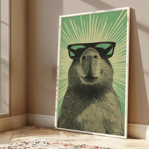 Peut inclure: Une impression d'art mural verticale encadr&eacute;e repr&eacute;sentant une illustration d&eacute;taill&eacute;e d'un capybara portant des lunettes de soleil noires. Le capybara est centr&eacute; sur un fond vert clair avec des lignes rayonnantes vert fonc&eacute;.
