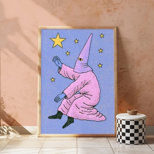 May include: A framed wall art print featuring a figure in a pink hooded robe with a single eye on the hood, reaching toward yellow stars against a textured light blue background. The figure has blue hands and black feet, depicted in a stylized illustration.