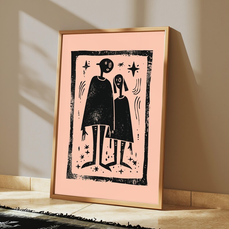 May include: A framed wall art print featuring a black ink illustration on a light peach background. The artwork depicts two stylized figures standing side by side within a textured rectangular border, surrounded by small star and curved line motifs.