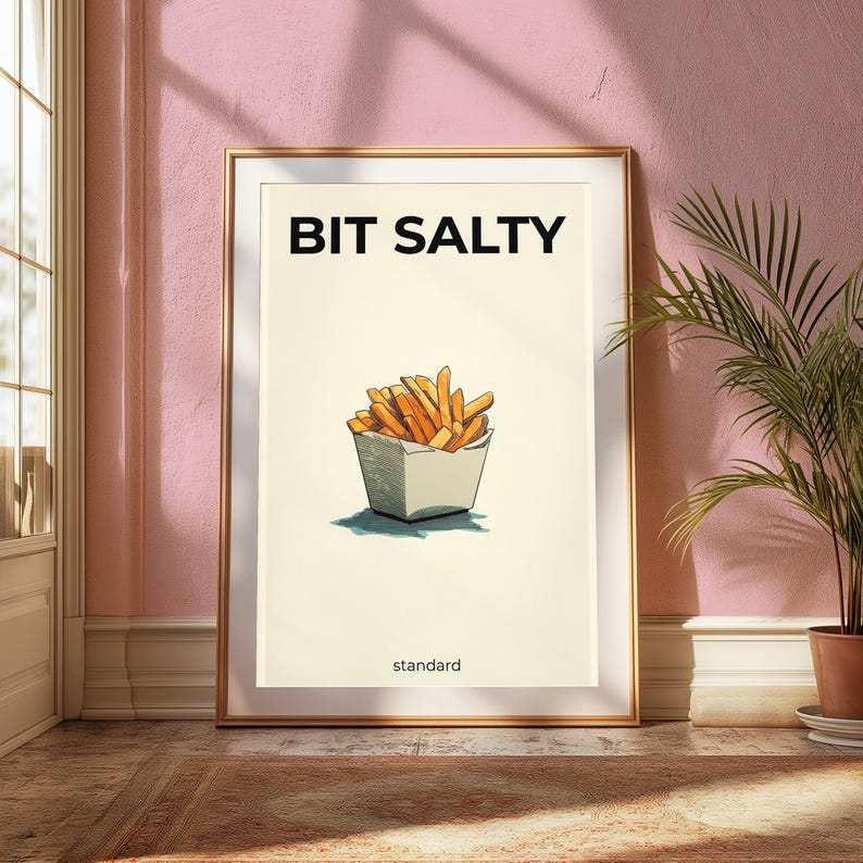 May include: A framed wall art print featuring a cream-colored background with a central illustration of golden-brown french fries in a white container. The text BIT SALTY appears in bold black letters above, with the word standard printed below.