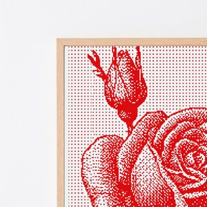 Pode incluir: Uma pe&ccedil;a de arte de parede emoldurada com um design de rosa vermelha pixelizada sobre um fundo branco. A obra exibe um bot&atilde;o de rosa detalhado e uma rosa parcialmente aberta criados com uma grade de pontos vermelhos, numa moldura de madeira clara.