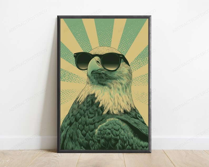 May include: A framed wall art print featuring a stylized illustration of a bald eagle wearing black sunglasses. The eagle is set against a background of alternating light green and tan sunburst rays with a subtle dotted texture throughout the design.