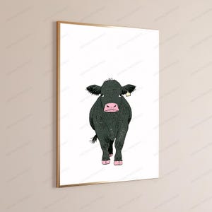 May include: A framed wall art print featuring a stylized illustration of a black cow with a pink nose and hooves, standing against a plain white background. The cow has a small yellow ear tag on its right ear and is rendered in a simple line art style.