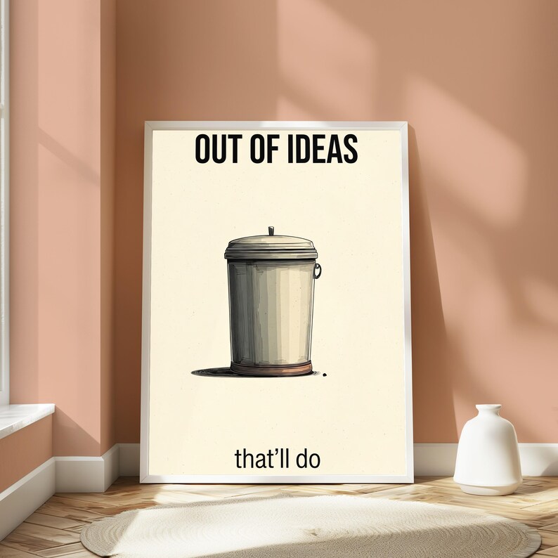 K&ouml;nnte beinhalten: Ein rechteckiger Wandkunstdruck mit cremefarbenem Hintergrund und einer zentrierten Illustration eines grauen Metallm&uuml;lleimers. Der Text OUT OF IDEAS ist oben in Schwarz gedruckt, und der Text that'll do ist unten in Schwarz gedruckt.