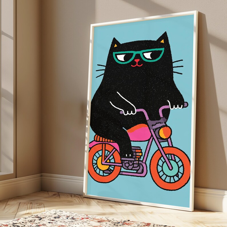 K&ouml;nnte beinhalten: Ein gerahmter Kunstdruck, der eine schwarze Katze mit t&uuml;rkisfarbener Brille auf einem Motorrad zeigt. Das Motorrad hat einen violetten Rahmen, leuchtend orangefarbene R&auml;der und einen pinken Sitz. Der Hintergrund ist ein hellblaues Feld.