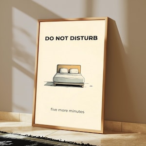 Puede incluir: Un cuadro enmarcado con una ilustraci&oacute;n de dibujos animados de una cama. Las palabras "DO NOT DISTURB" est&aacute;n en la parte superior, y "five more minutes" en la inferior. El marco es de color marr&oacute;n claro.